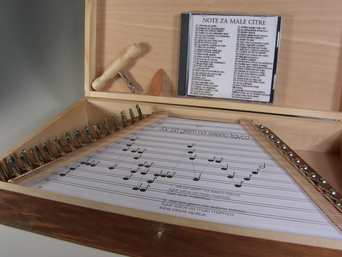 Cítara- Instrumento de 15 cuerdas dobles de dos octavas. Se presenta en una caja de madera con 60 plantillas de canciones populares eslovenas y un CD.